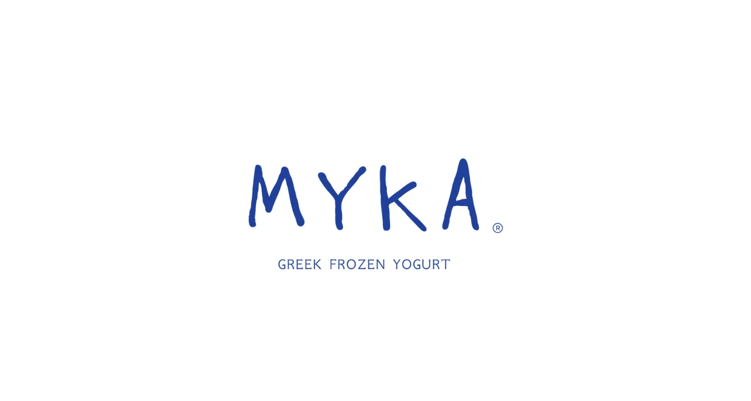 Fachada de Myka San Lucas con rótulo azul iluminado y entrada cálida en tonos arena con detalles vegetales.
