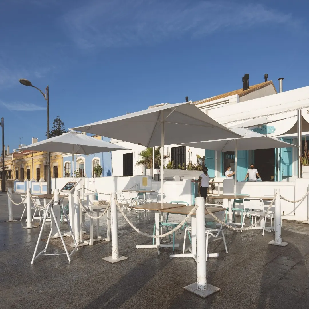 Sombrillas blancas, sillas turquesa y luz mediterránea en la terraza de La Más Bonita. Ideal para un desayuno frente al mar.