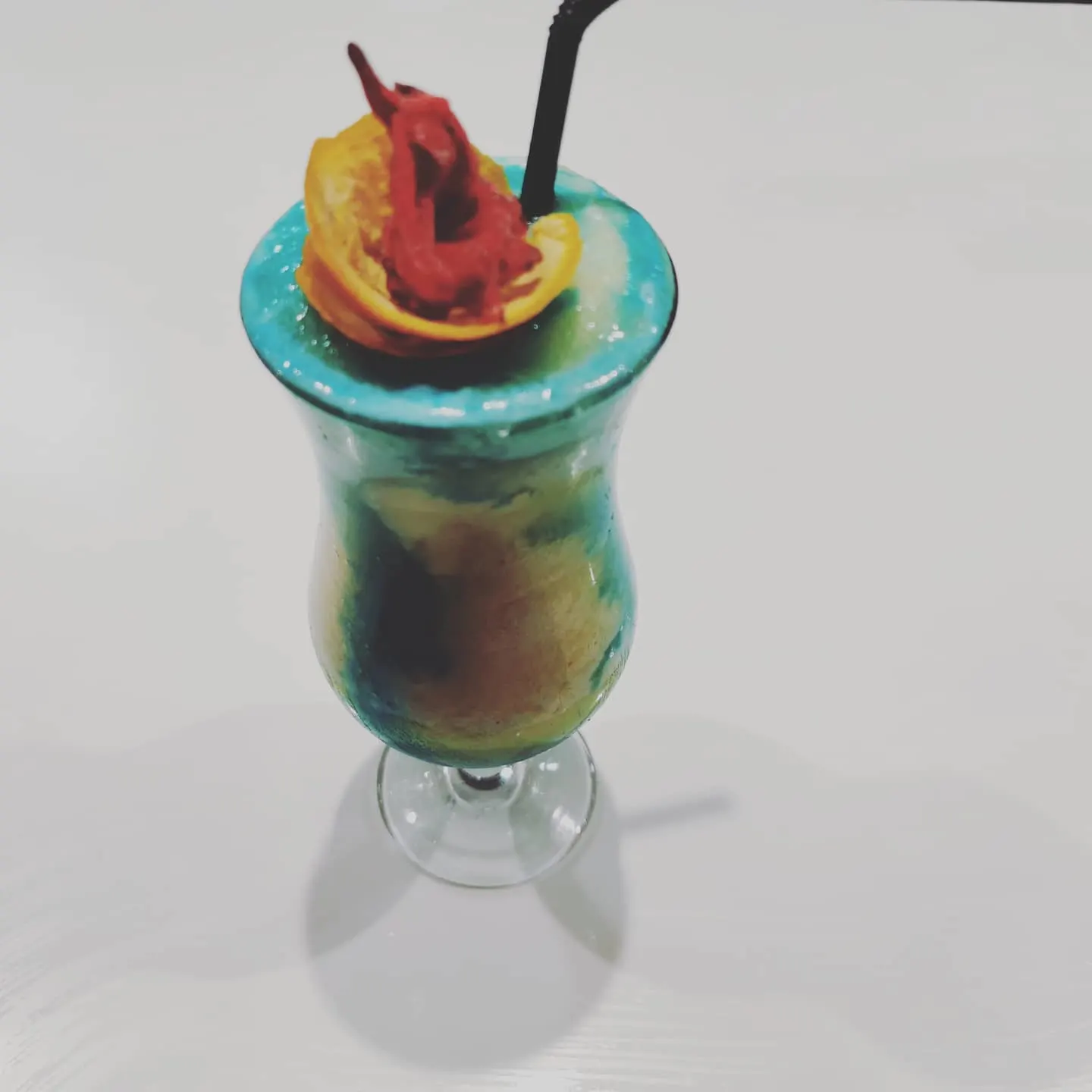 Cóctel colorido en Artadi Beach con tonos azules, decoración de frutas y pajita negra. Ambiente refrescante y tropical.