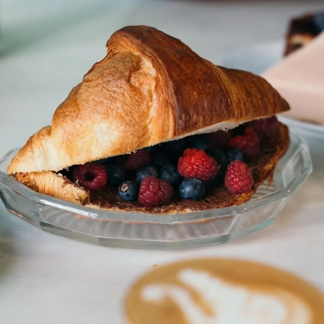Croissant abierto relleno de frambuesas y arándanos sobre plato de cristal, presentado con estilo sencillo y apetitoso.
