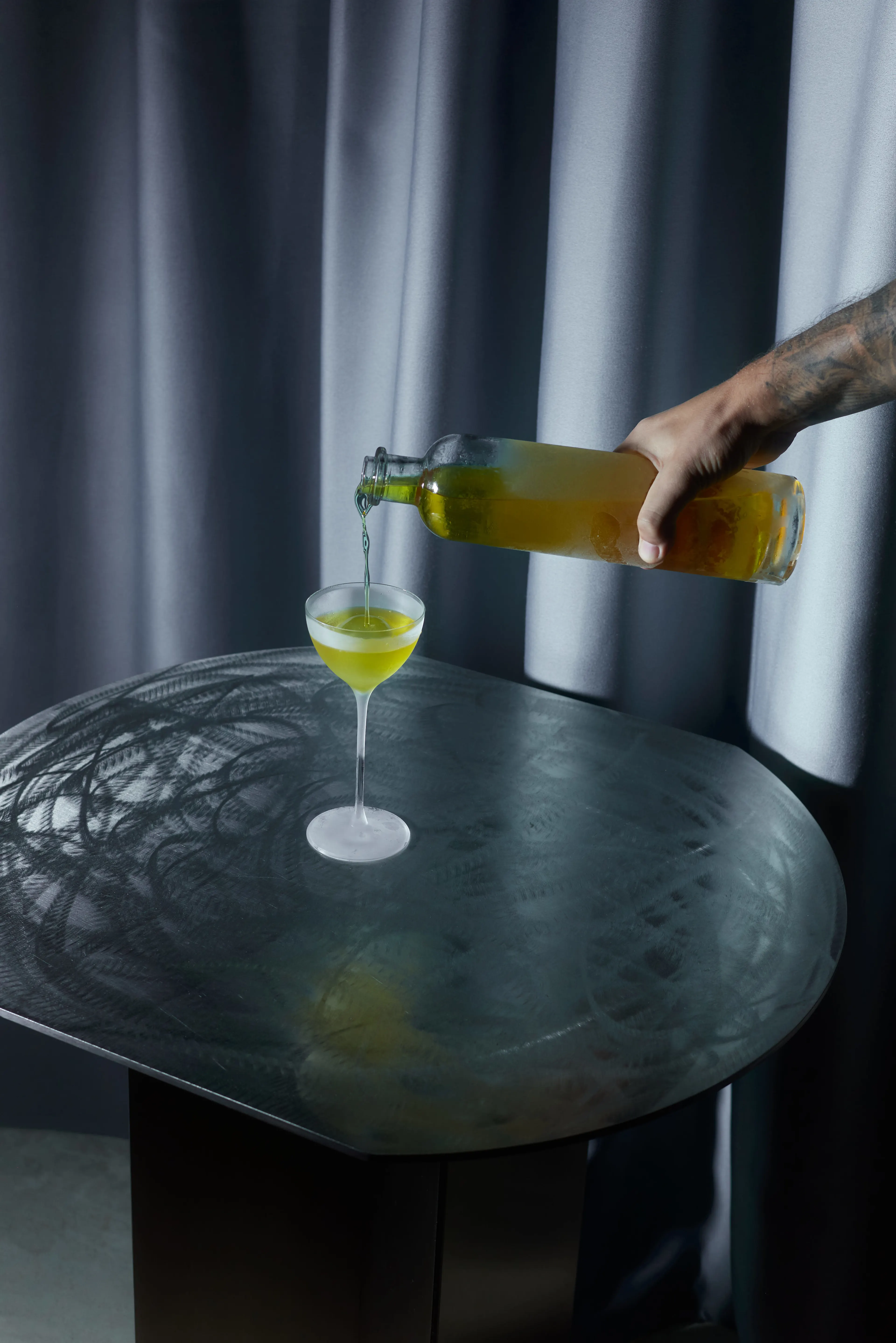 A cocktail being poured from a glass bottle into a fancy cocktail glass.