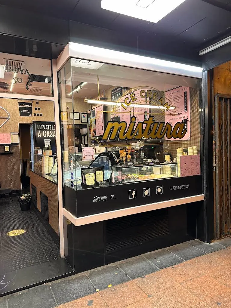 Fachada acristalada de Mistura Goya con logo dorado, mostrador de helados a la vista y cartelería rosa que invita a entrar.