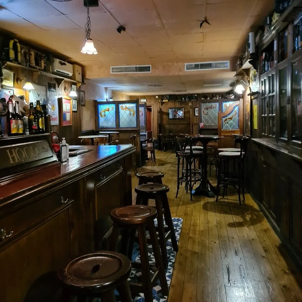 Entrada verde del pub Robin Hood con letras doradas, tres lámparas vintage y una mesa alta con cenicero en la puerta.