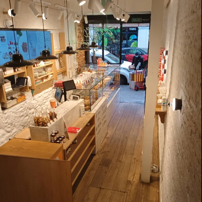 Vista del interior al acceso de Maison Kayser Fernando VI, con mostrador de dulces, suelos de madera y decoración rústica e industrial.