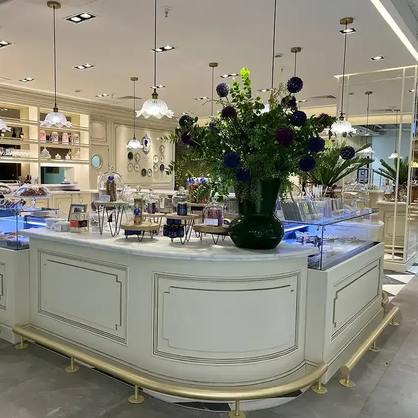 La barra del Café Bistrot Isabel Maestre brilla con vitrinas iluminadas, flores frescas y una cuidada estética clásica con molduras, dorados y lámparas colgantes.
