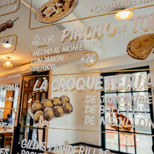 Detalle del cristal de Bareto con ilustraciones y nombres de tapas como croquetas de jamón, boletus o mejillón, y su famoso pincho de tortilla hecho al momento.