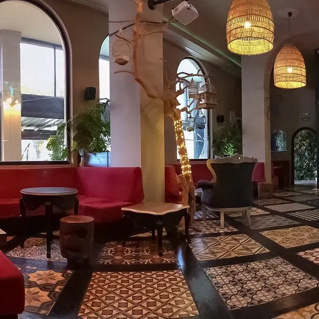 Bohra Shisha Cocktail destaca por su suelo decorativo, sofás rojos y detalles elegantes como lámparas tejidas y árboles iluminados.