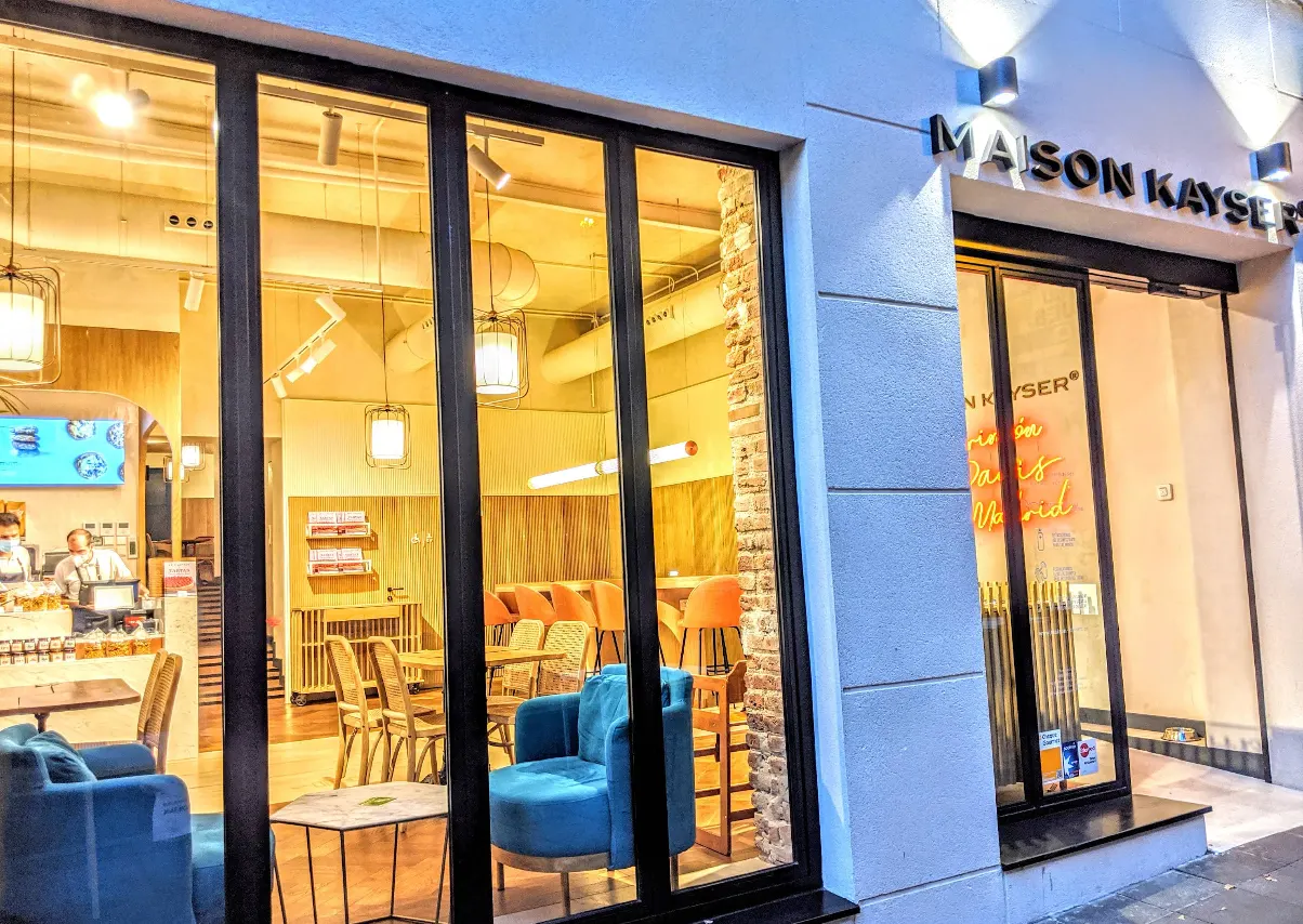 Fachada acristalada de Maison Kayser en Velázquez, con interior cálido y diseño moderno visible desde la calle.