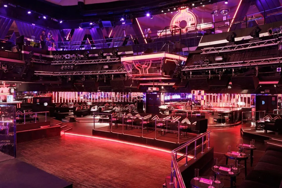 Sala principal de Teatro Barceló vacía, iluminada con luces rosas y violetas, con zonas VIP, barras de bar, cabina de DJ elevada y decoración moderna.Interior de discoteca moderna con luces de neón, varios niveles y zonas de asientos.
