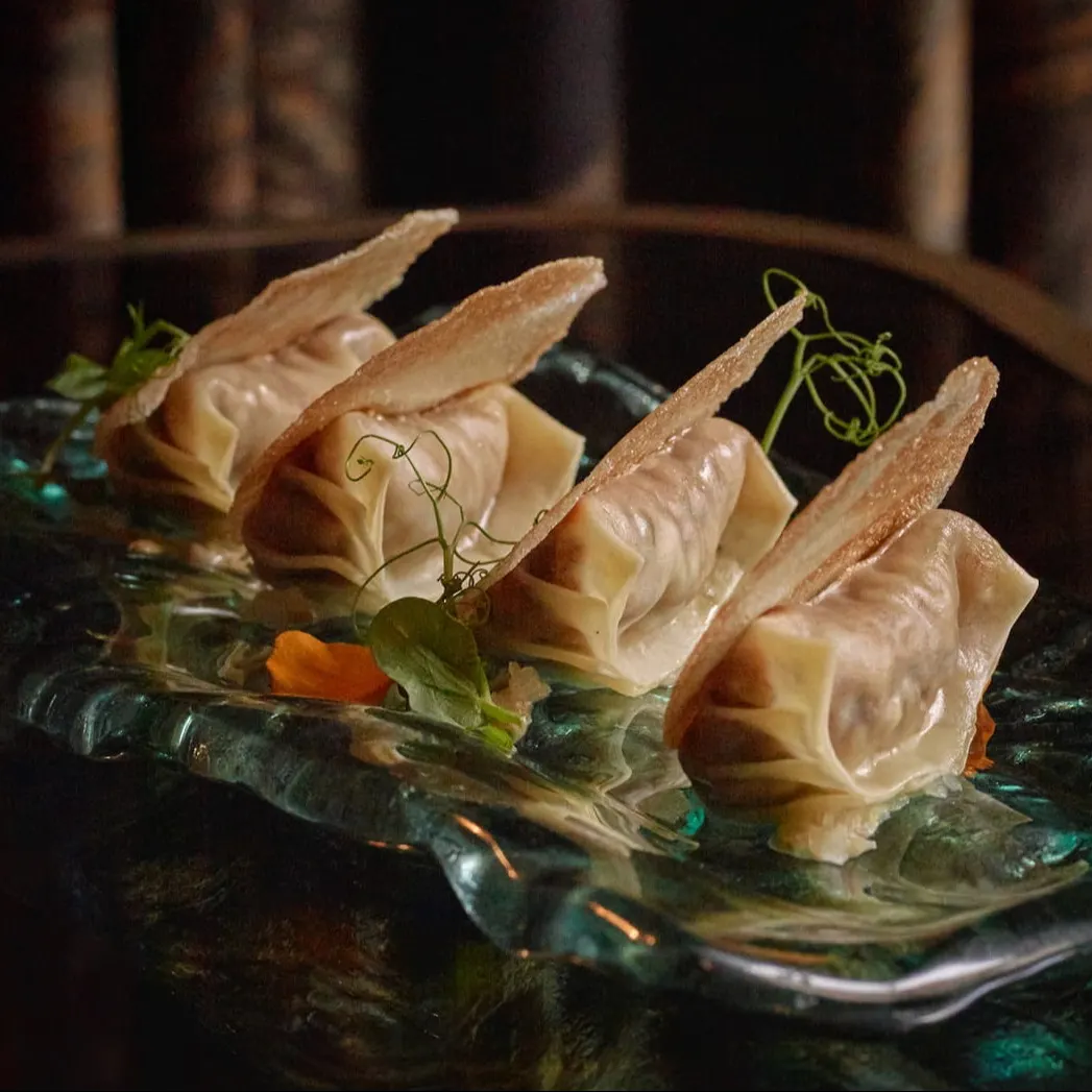 Deliciosos dumplings servidos en Isa Restaurant & Bar, acompañados de chips crujientes y un toque de frescura vegetal. Un bocado de alta cocina.