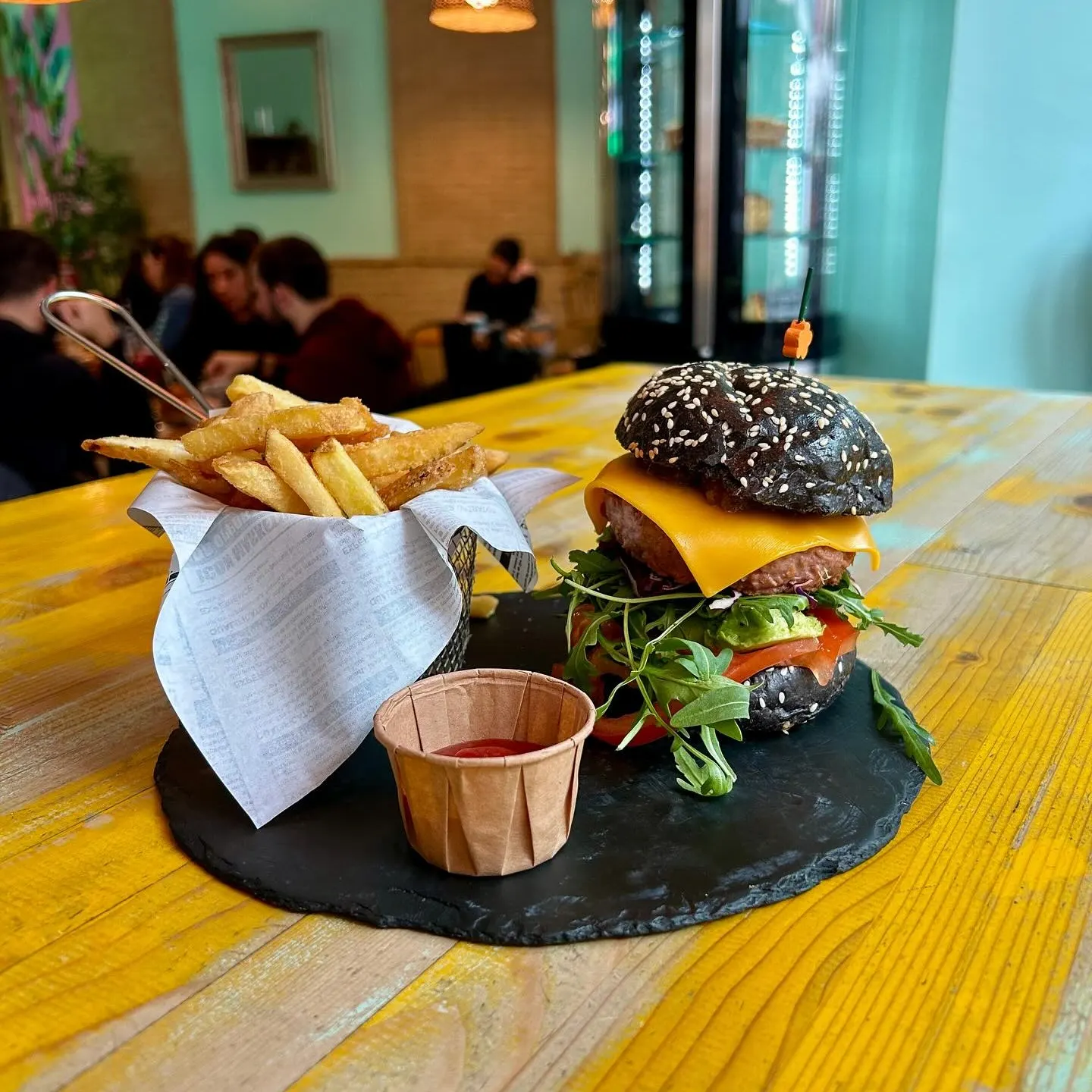 Plato de La Mala Brunch con hamburguesa de pan negro, queso cheddar, lechuga, tomate, papas fritas y salsa sobre bandeja de pizarra.