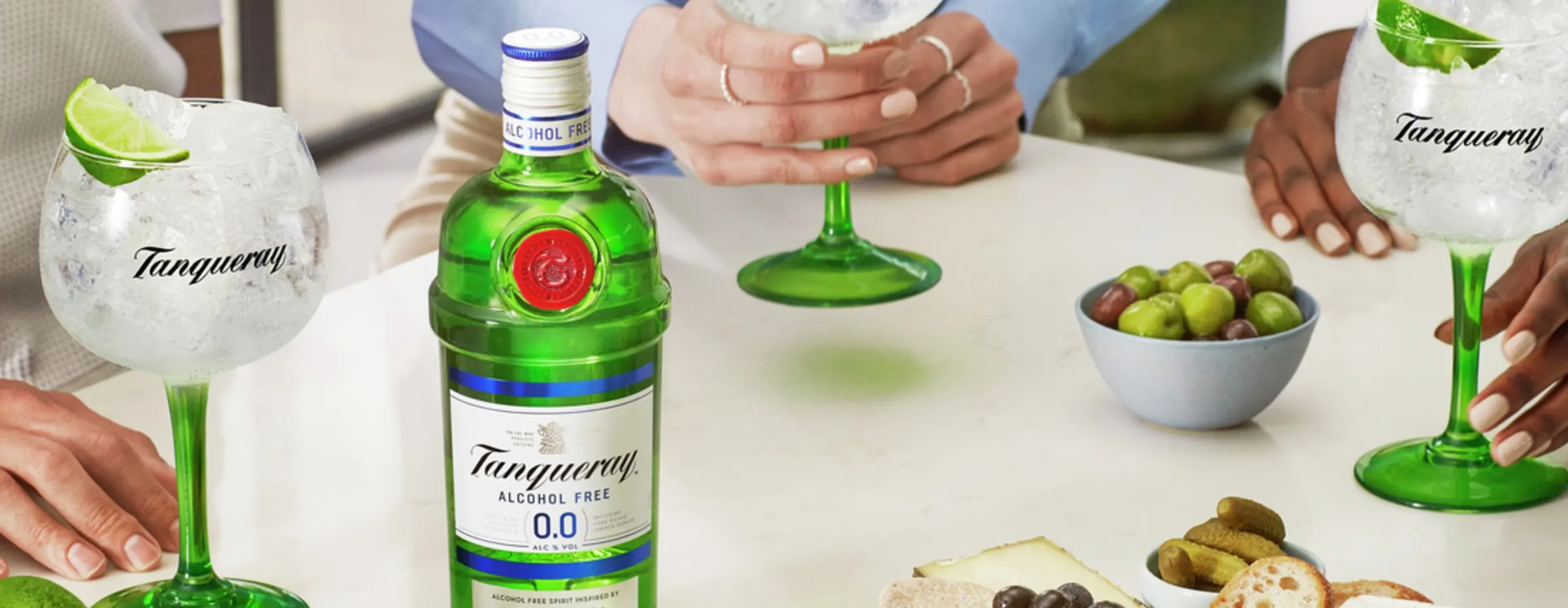 Varias copas de gin tonic con rodajas de lima y una botella de Tanqueray sin alcohol sobre una mesa con aperitivos.