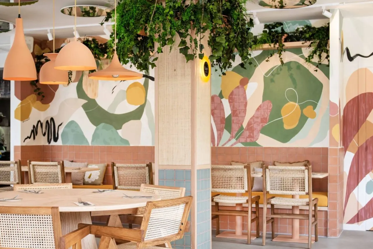 Interior de Mood Brunch con paredes decoradas con murales coloridos, lámparas colgantes color terracota y mesas de madera con sillas de mimbre.