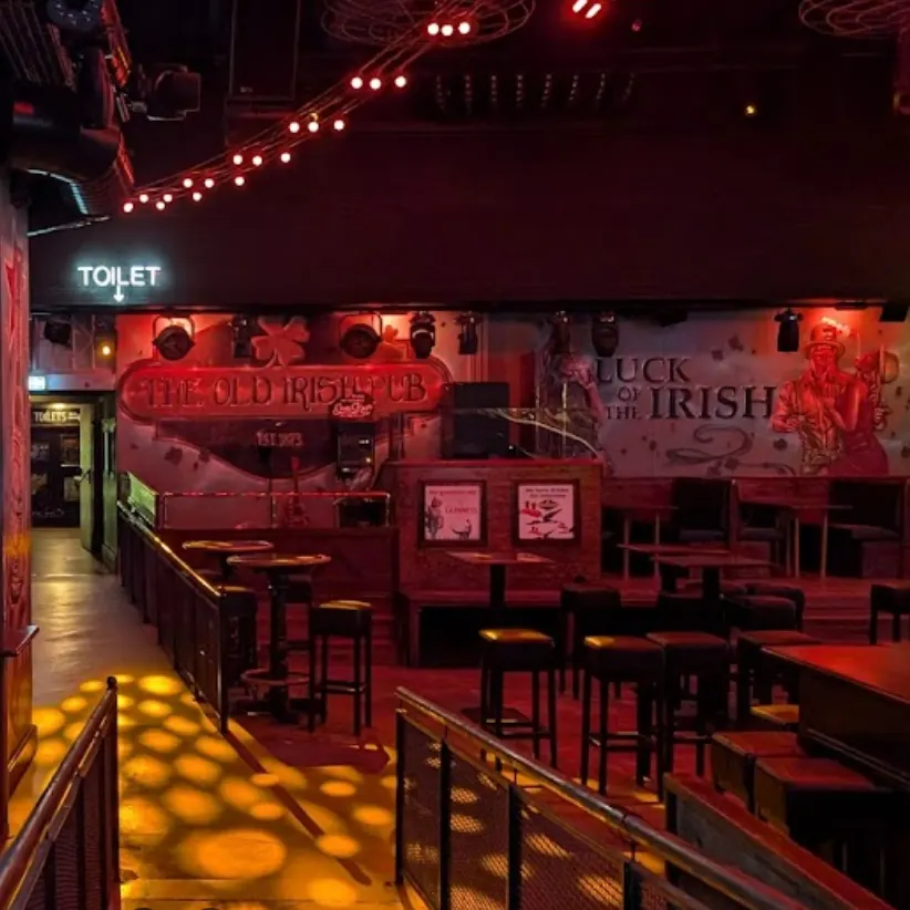 The Old Irish Pub presenta un ambiente acogedor con luces cálidas, murales temáticos irlandeses y mobiliario rústico ideal para noches animadas.