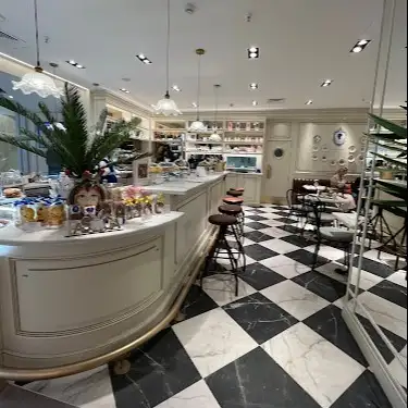 Interior elegante de Café Bistrot Isabel Maestre con suelos de mármol, barra blanca curvada, lámparas colgantes y una cuidada decoración clásica y floral.