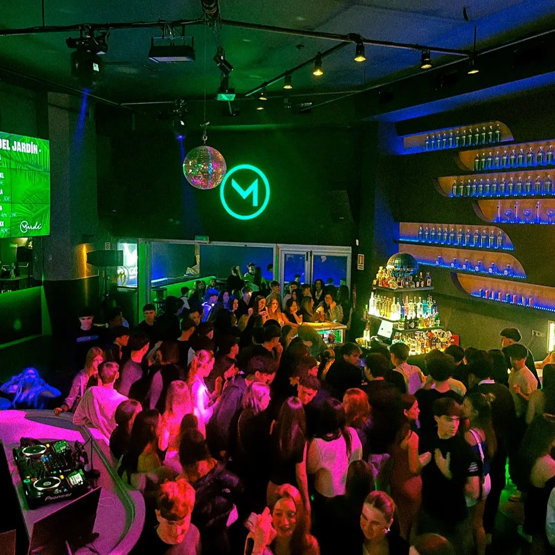 Multitud en la pista de Mardé con luces verdes, cabina de DJ iluminada y botellas alineadas tras la barra.