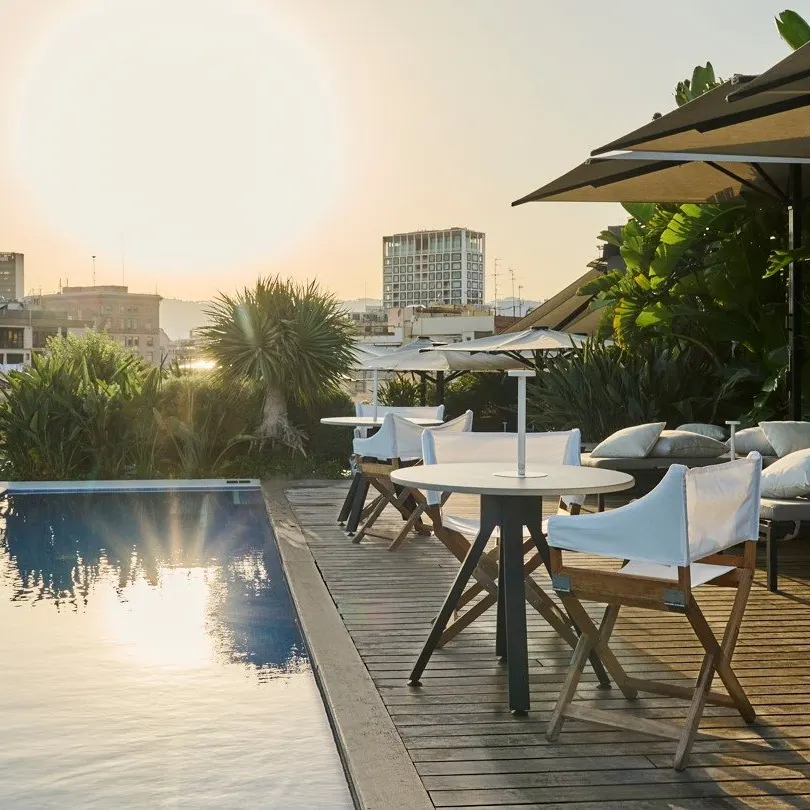 Terraza con piscina, mesas, sombrillas y vistas panorámicas de la ciudad al atardecer en Mood Rooftop Bar, creando un ambiente relajado y moderno.