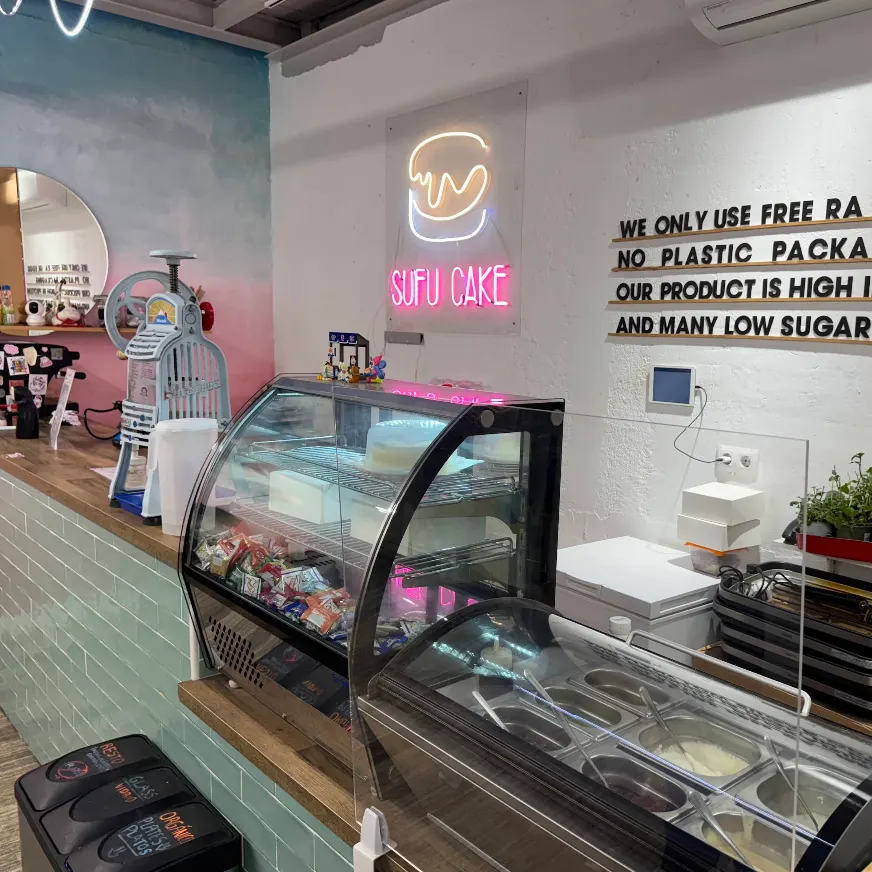 Vitrina con helados y pasteles en Sufu Cake junto a una barra rosa y azul en un espacio creativo y colorido.
