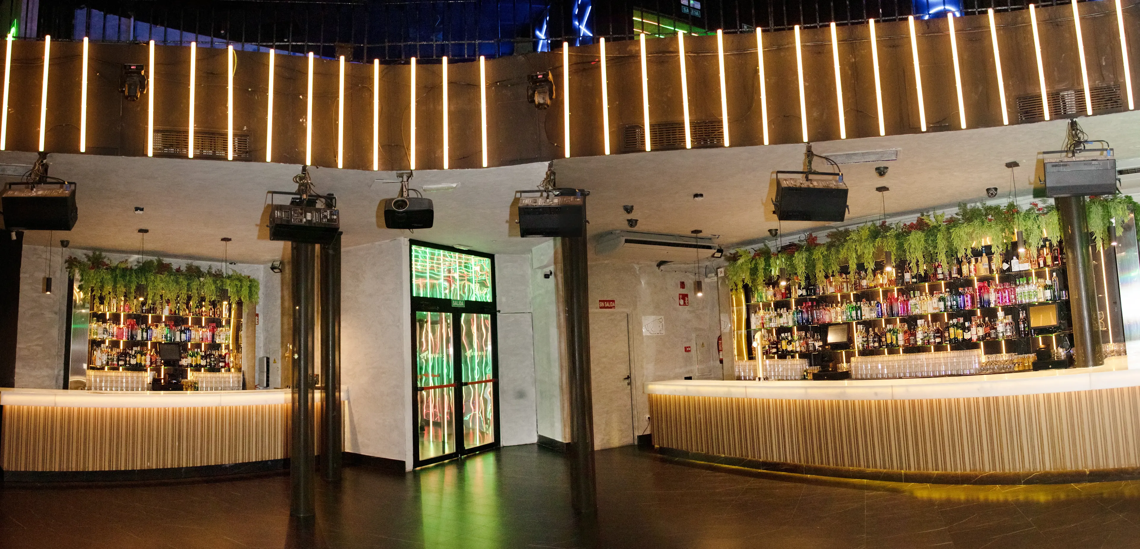 The Bar | Sala Jerusalem - Vista panorámica del bar principal de la Sala Jerusalem, mostrando la amplia barra iluminada y decorada con vegetación colgante.