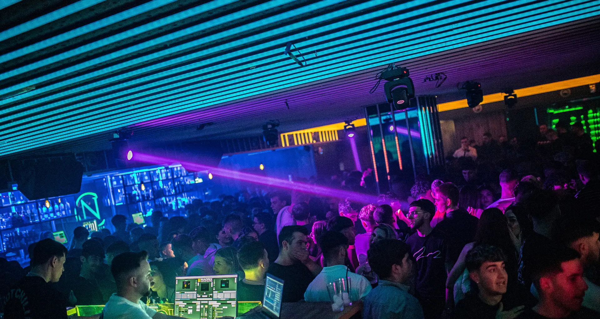 Coltán y Benavente con luces neón, DJ en acción y una multitud animada, creando una noche vibrante y llena de ritmo.
