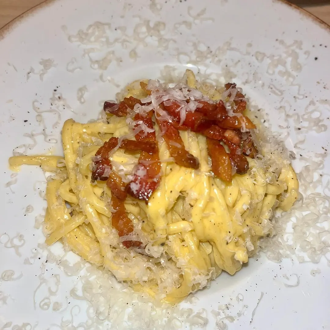 Pasta carbonara con salsa cremosa, guanciale crujiente y queso rallado, servida con un toque de pimienta en un plato de estilo rústico.