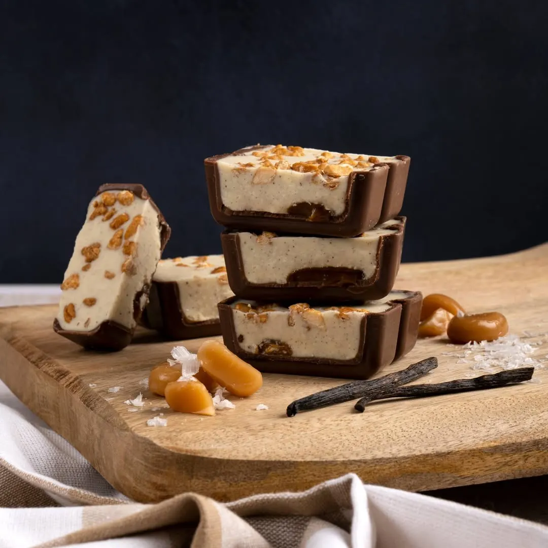 Bombones de helado de vainilla con cobertura de chocolate, crocante por encima y toques de caramelo sobre tabla de madera en Torrons Vicens.