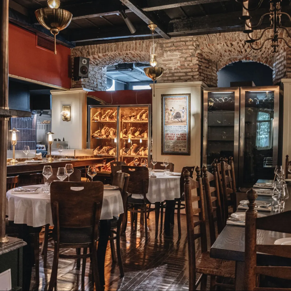Salón cálido y elegante en Madre, con vitrinas llenas de carne madurada, luz tenue y mesas preparadas para disfrutar de una experiencia gastronómica impecable.