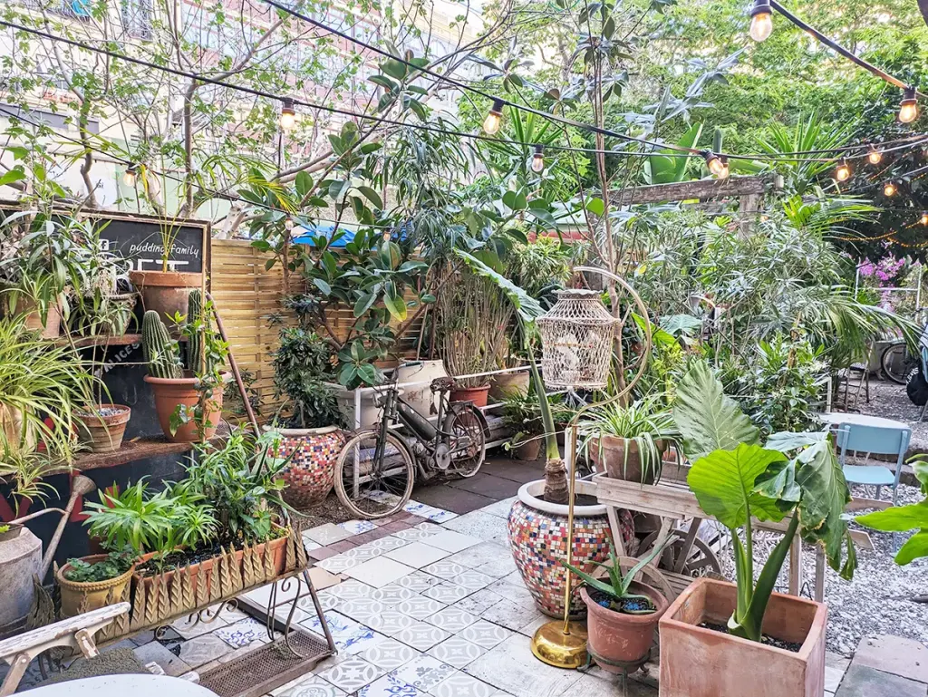 Terraza de Alice Secret Garden con mesas entre árboles, guirnaldas de luces y una gran seta decorativa en el centro del espacio.