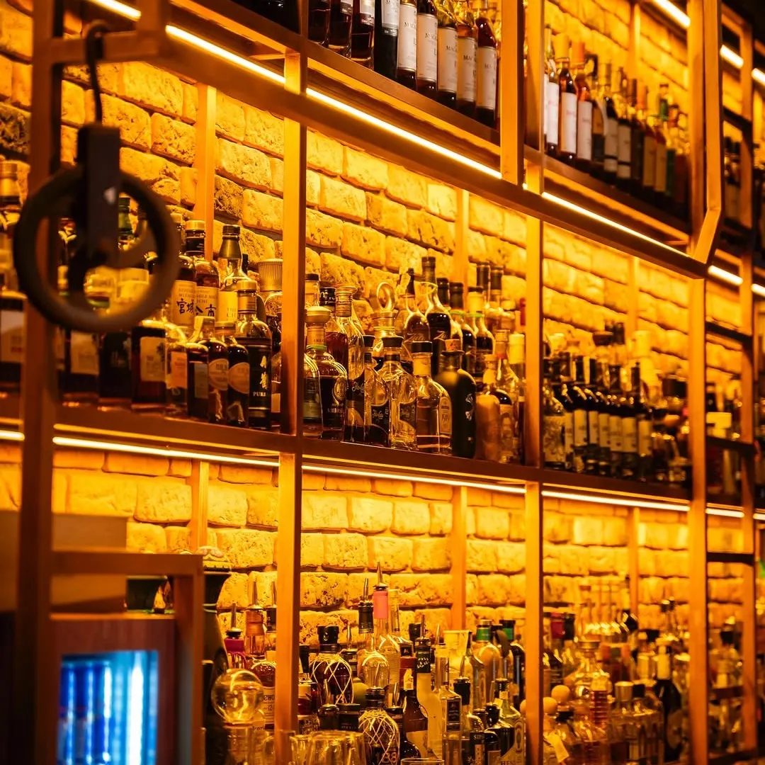 Primer plano de estanterías con botellas y fondo de ladrillo naranja, iluminado con luz cálida en Grog Santander.