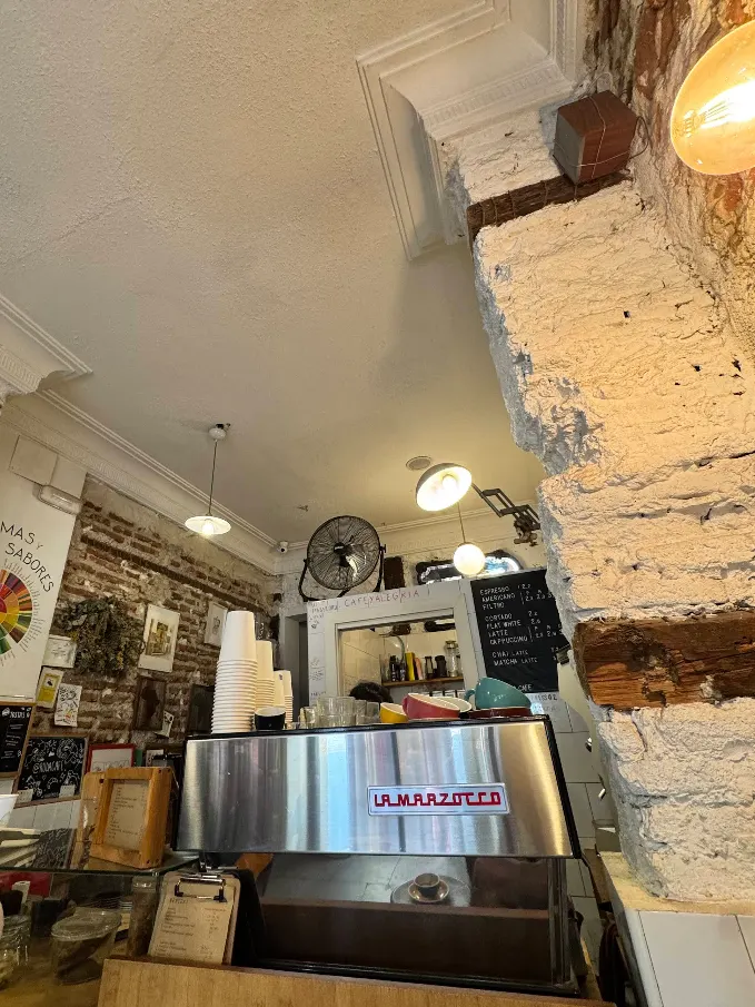 Interior de Ruda Café con paredes de ladrillo visto, máquina La Marzocco en primer plano y detalles rústicos que crean un ambiente acogedor y auténtico.