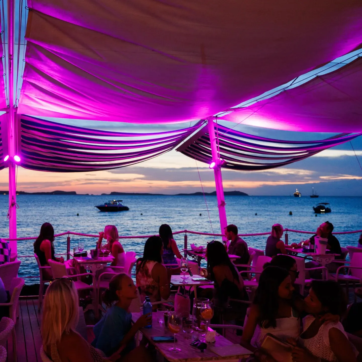 Terraza de Café del Mar en Ibiza, con vistas al mar al atardecer, luces púrpuras y ambiente relajado para disfrutar de cócteles únicos.
