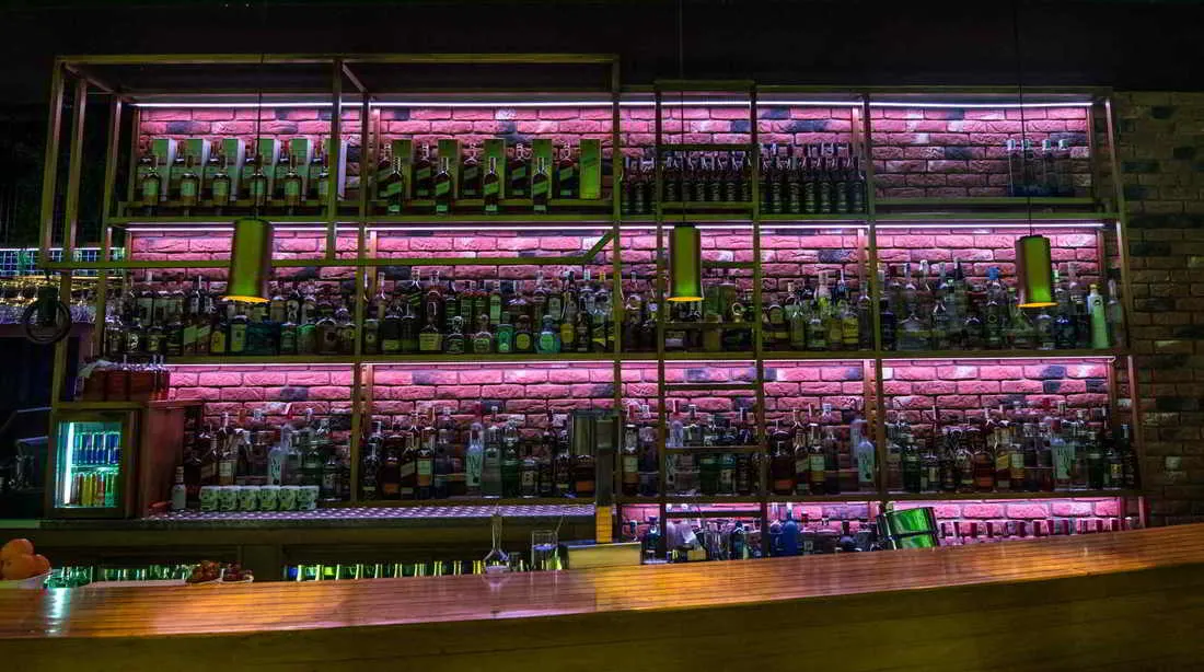 Estanterías con botellas iluminadas en rosa sobre pared de ladrillo visto y barra de madera en el bar Grog Santander.