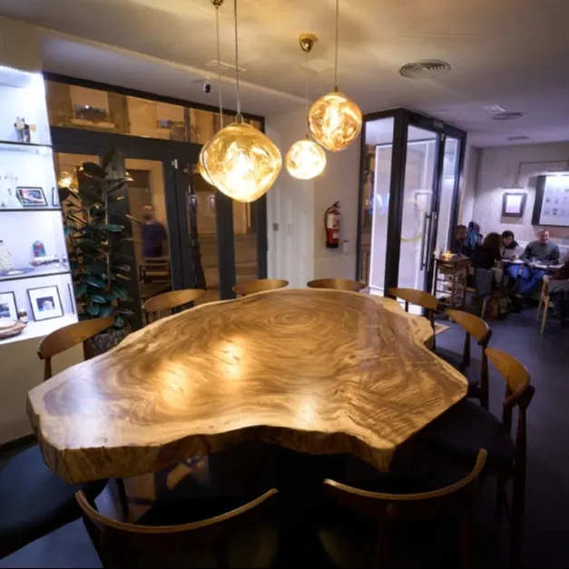 The Bar | Moonlight Experimental Bar - Vista del salón principal con una mesa central de madera y lámparas colgantes, mostrando un ambiente acogedor y moderno.