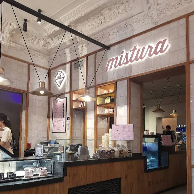 Zona de servicio en Mistura Plaza del Ángel con techos ornamentados, barra en madera clara y detalles gráficos de helado en las paredes.