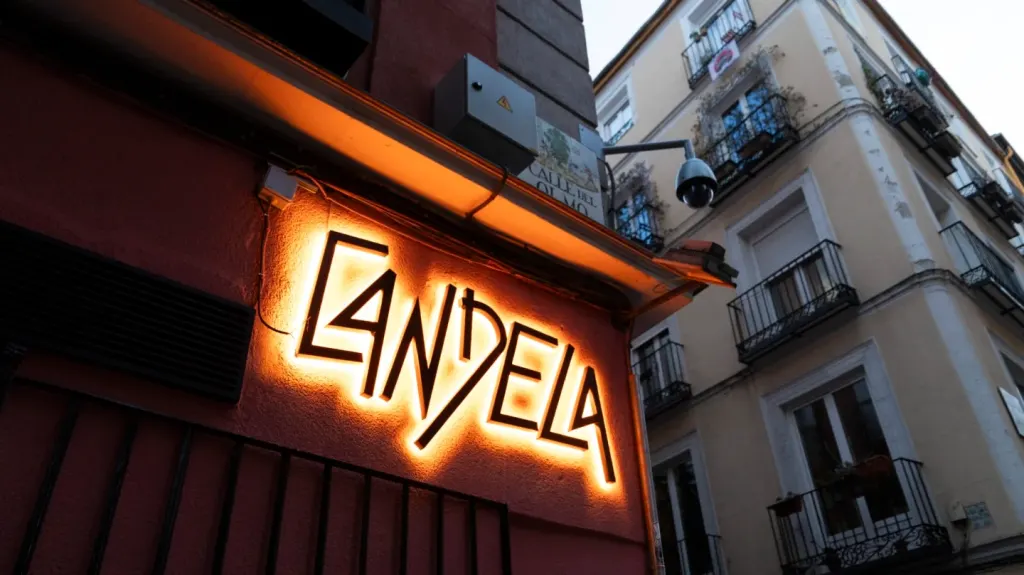 Cartel luminoso de El Candela encendido al anochecer sobre la fachada rojiza, con el nombre en letras inclinadas y la esquina de Lavapiés al fondo.