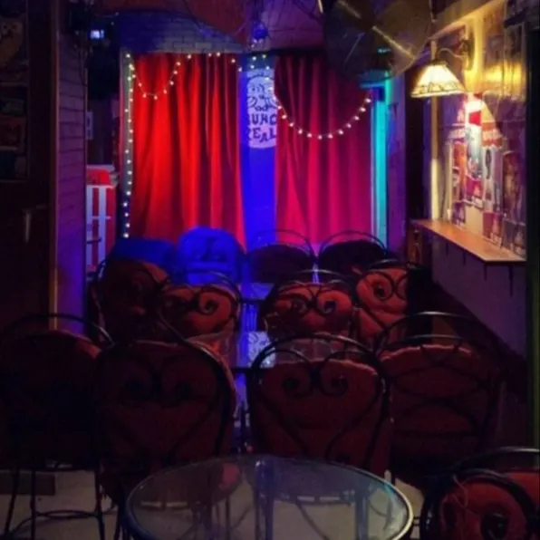La imagen muestra el interior de la Sala Buho Real, con un escenario. El escenario está enmarcado por cortinas rojas y tiene un letrero que dice “BUHO REAL”.