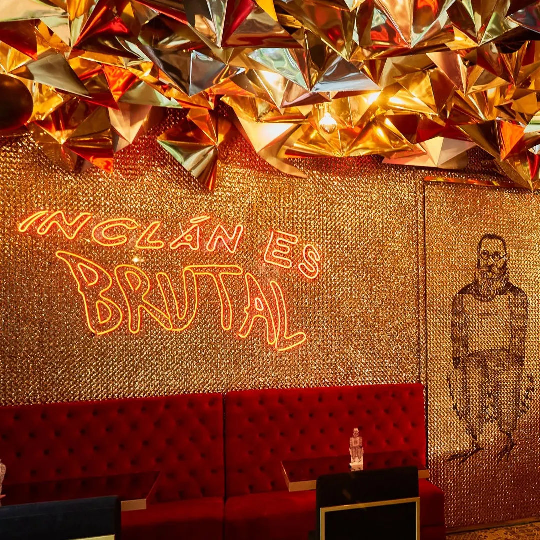 En Inclán Brutal Bar, paredes doradas reflejan un estilo extravagante, con sofás rojos y un letrero de neón que declara su brutalidad.