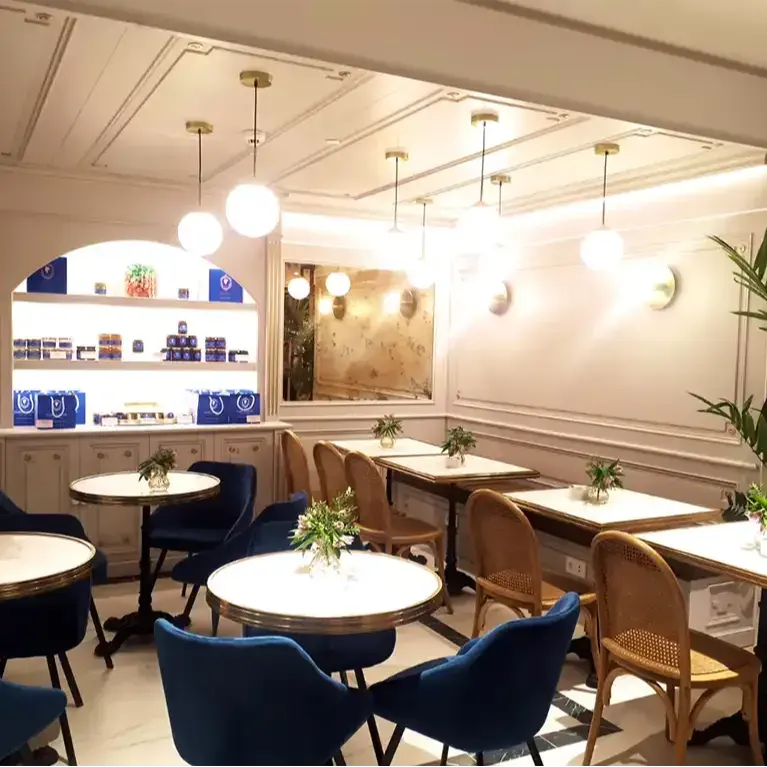 Mesas con flores, sillas de terciopelo azul y mimbre, lámparas esféricas y una estantería iluminada crean un ambiente sofisticado en Isabel Maestre Goya.