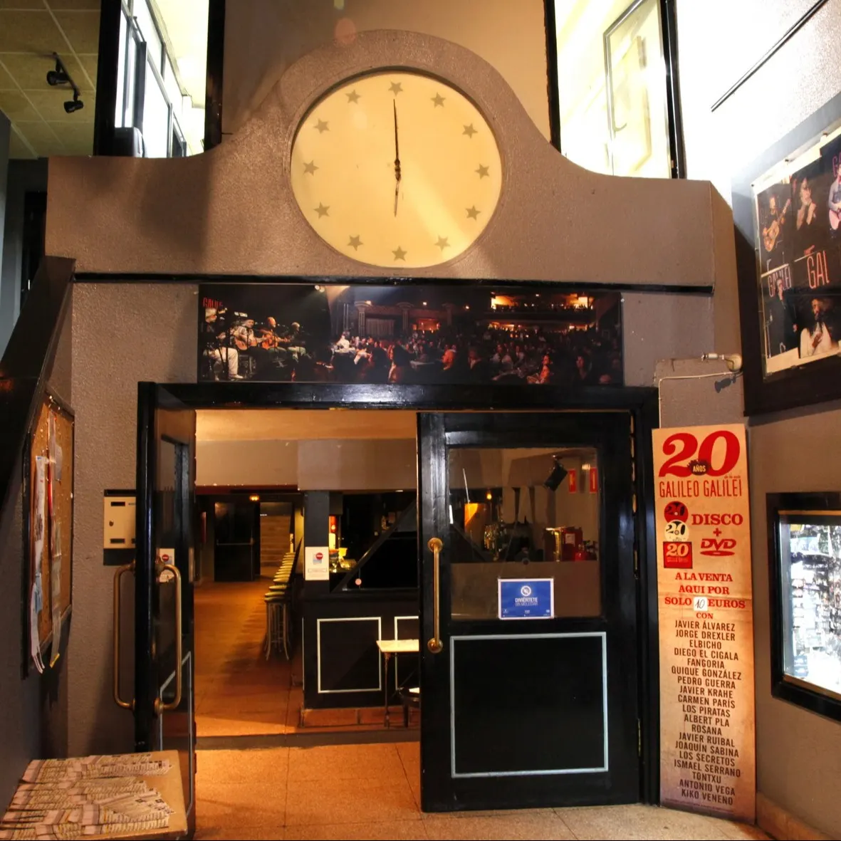 Entrada de la sala Galileo Galilei con puertas abiertas, decorada con fotos de actuaciones, un reloj clásico y carteles promocionales de eventos.