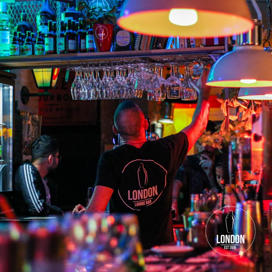 Entrada del bar London con su logotipo iluminado en naranja sobre madera y vistas del interior con luces de neón y referencias a Tanqueray.