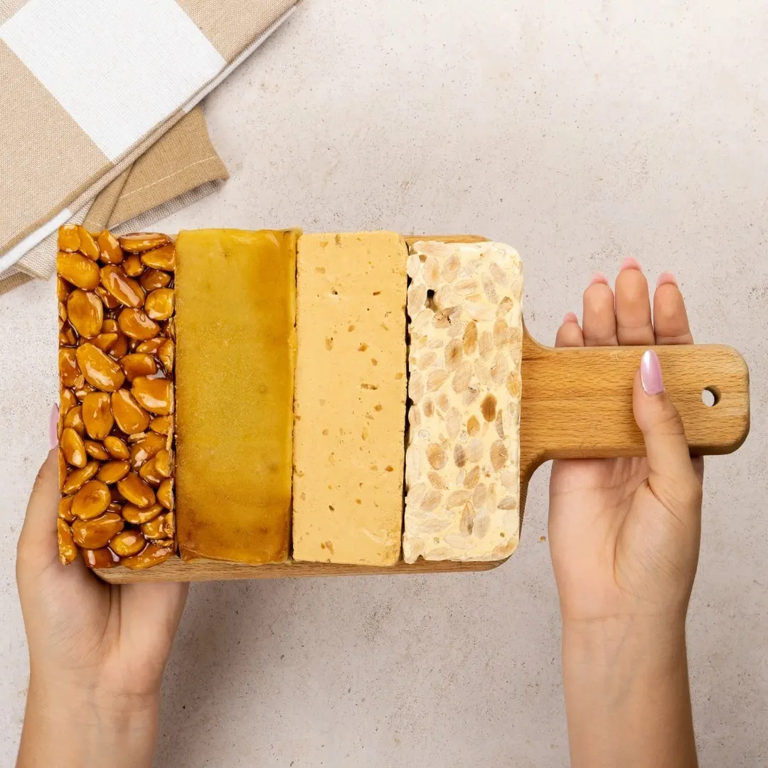 Selección de turrones clásicos con diferentes texturas y colores alineados sobre tabla de madera en Torrons Vicens.