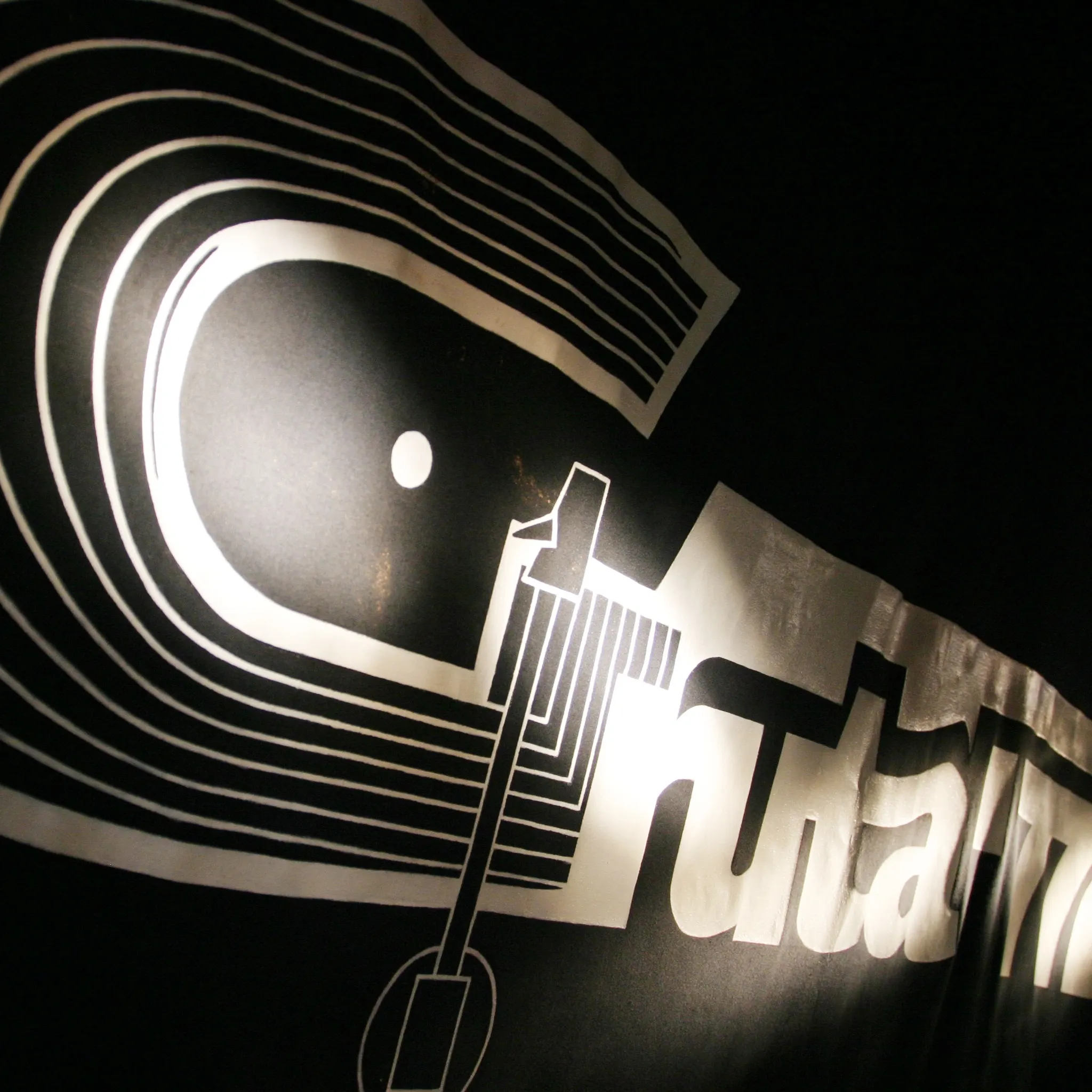 Logotipo en blanco y negro de Gruta 77, con diseño inspirado en vinilos y líneas curvas iluminadas sobre un fondo oscuro.