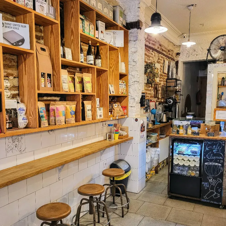 Estanterías de madera repletas de productos artesanales y taburetes altos en Ruda Café, un espacio cálido con ladrillo visto y detalles cuidados.