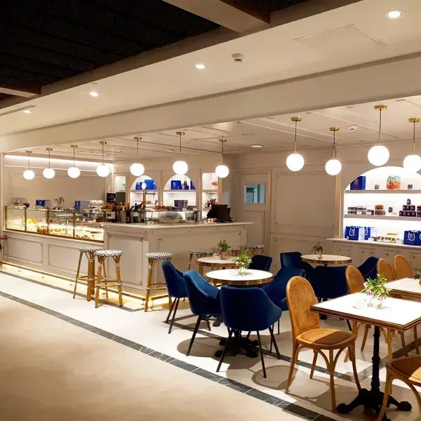 El Café Bistrot Isabel Maestre en Goya destaca con sillas azul intenso, mesas con flores frescas, lámparas esféricas y una barra iluminada de estilo clásico.