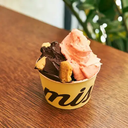 Tarrina de helado en Mistura calle de Toledo con dos sabores artesanos y trozos de galleta sobre una mesa de madera.