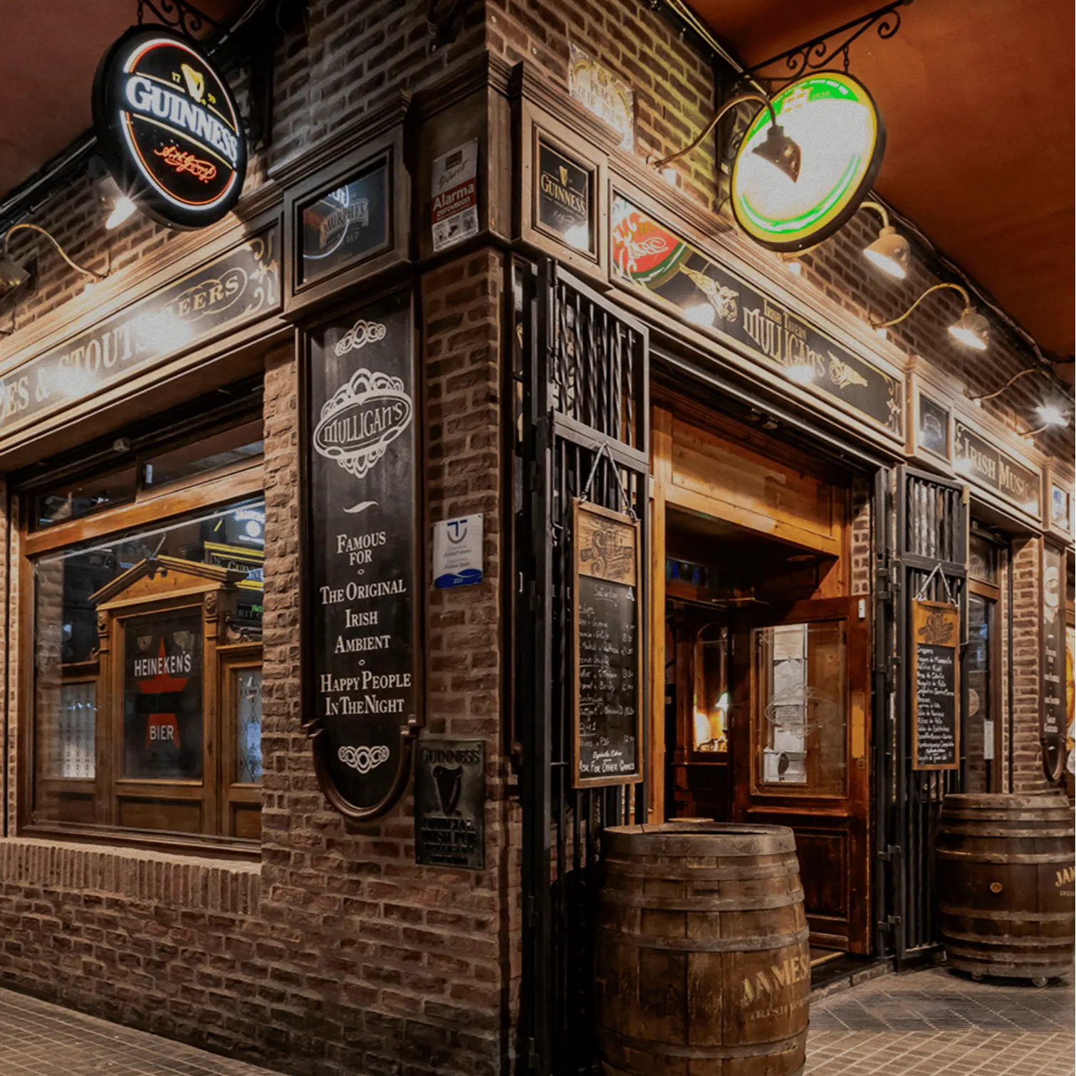 Fachada de ladrillo de un pub irlandés, con carteles de Guinness, toneles de madera y luz cálida iluminando la entrada.