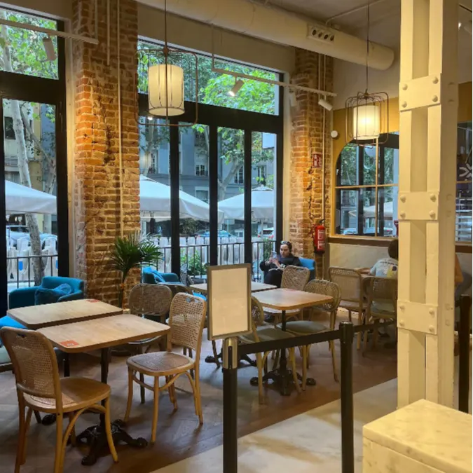 Espacio de degustación en Maison Kayser Velázquez con luz natural, muros de ladrillo visto y terraza exterior al fondo.