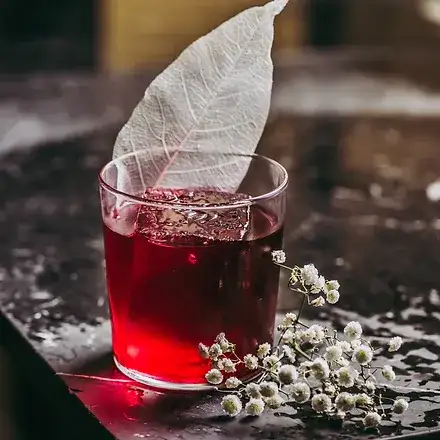 En Farola, un cóctel rojo intenso con una hoja blanca decorativa y flores delicadas crea una experiencia visual y gustativa única.