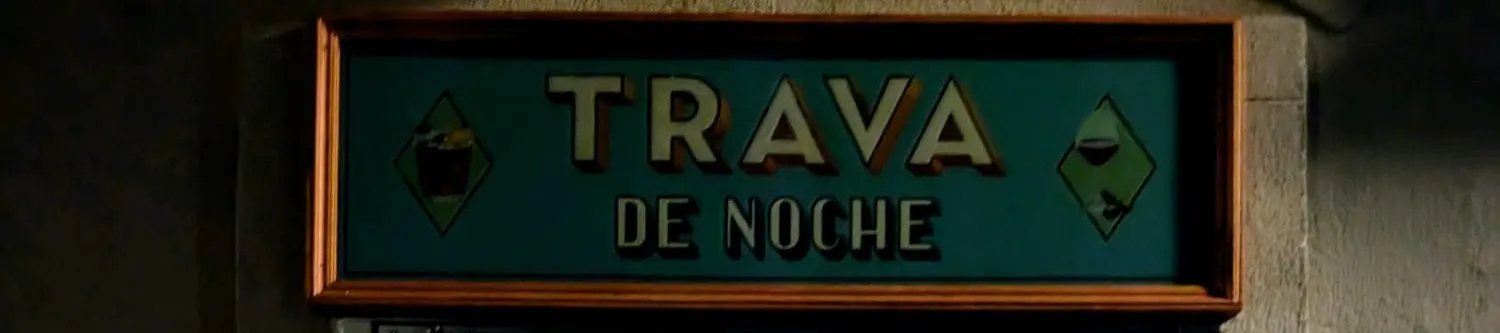 Cartel retroiluminado de Trava de Noche con marco de madera, fondo verde y letras en relieve, acompañado por ilustraciones de cócteles a cada lado.