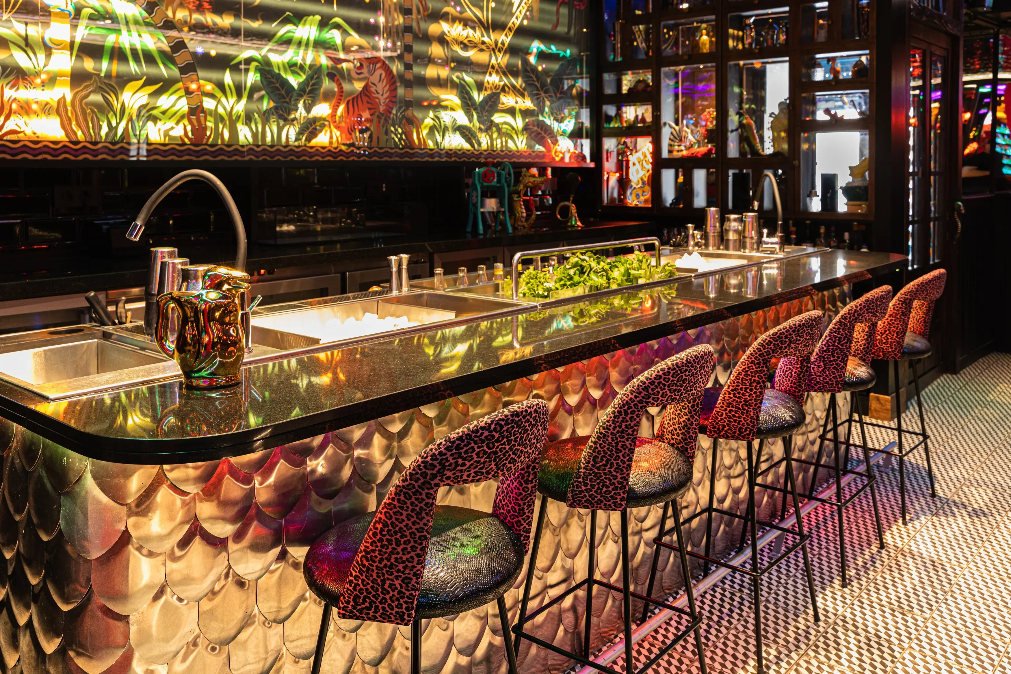 Barra iluminada con sillas de estampado animal en tonos rojos y un fondo decorado con motivos selváticos y neón brillante